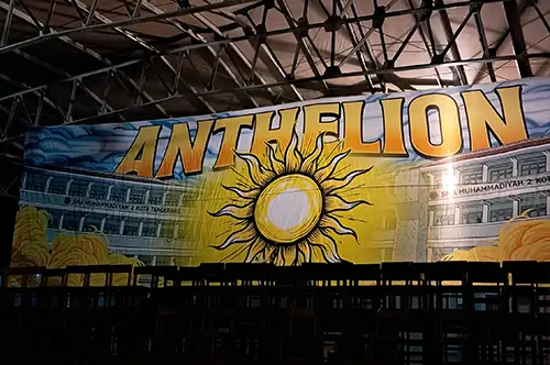 Bendera custom berukuran besar dengan desain tulisan ANTHELION dan ilustrasi matahari terpasang di dalam gedung, hasil cetak berkualitas dari Nusaflag.